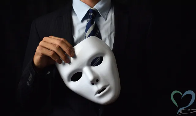 仮面を片手に持つスーツの男性